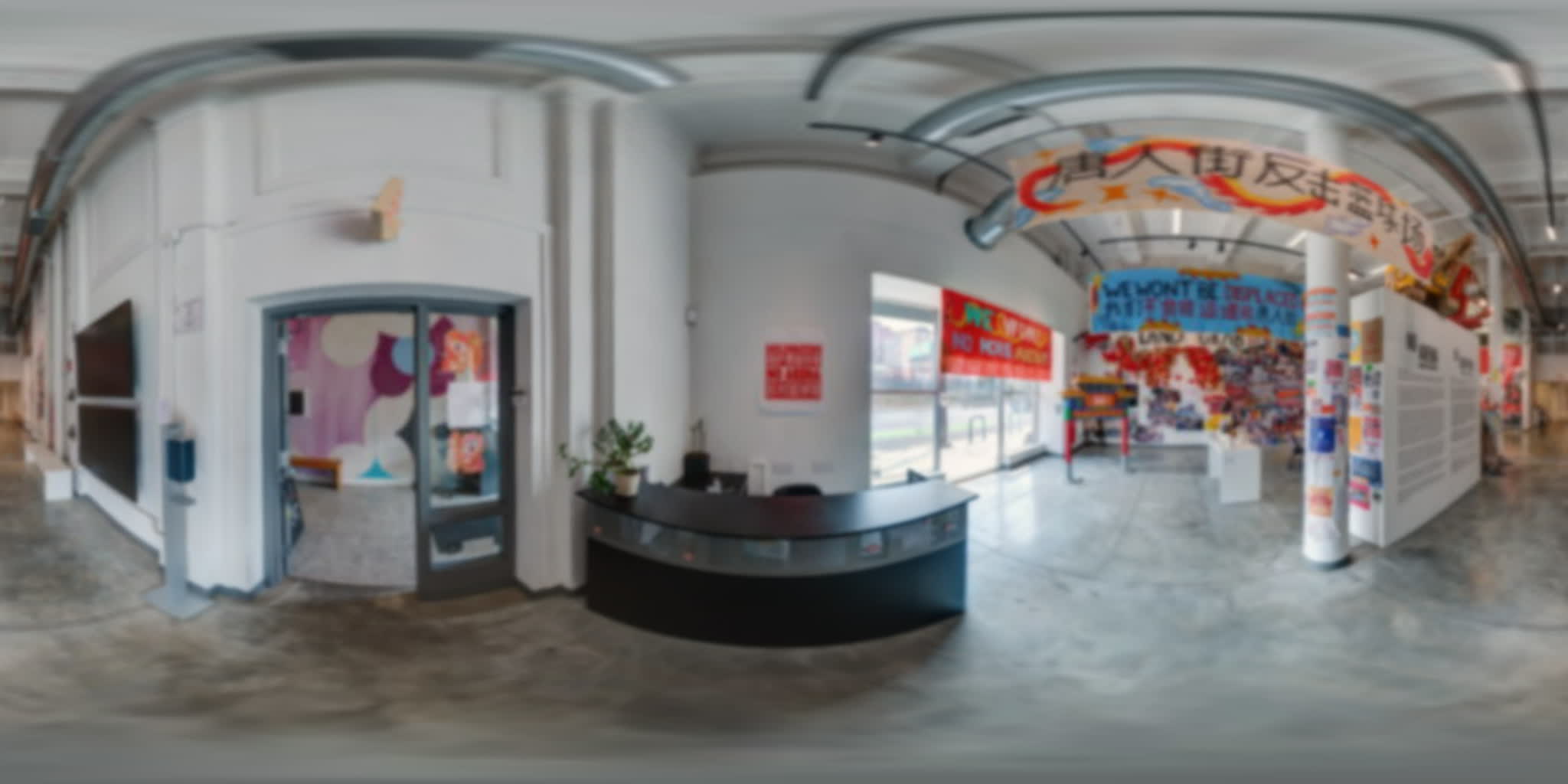 Reception area with a curved desk, banners, protest art, and an open view into the gallery.