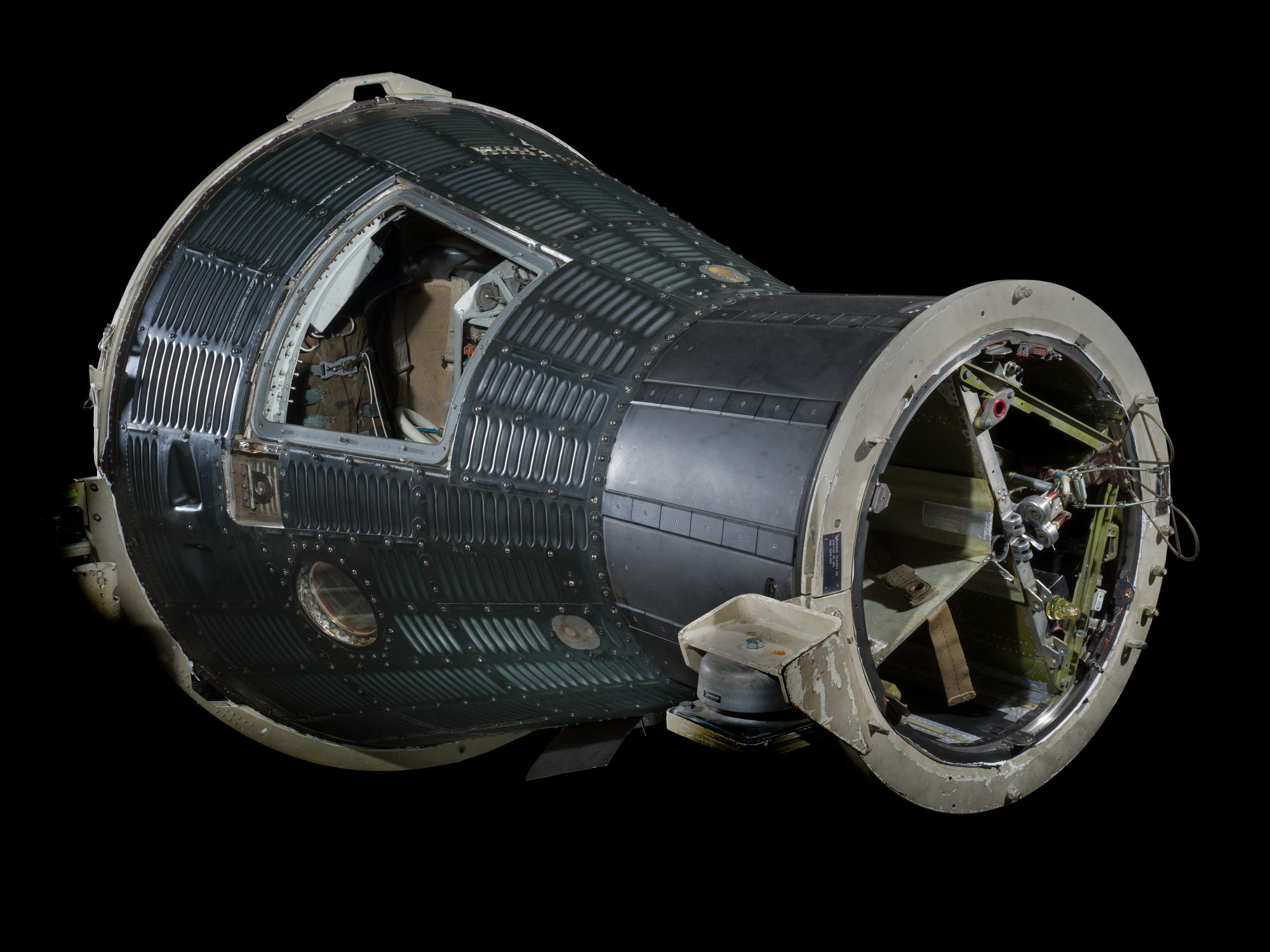 Dark corrugated conical Mercury capsule with a clear replacement hatch revealing the single seat and dense instrument panel.