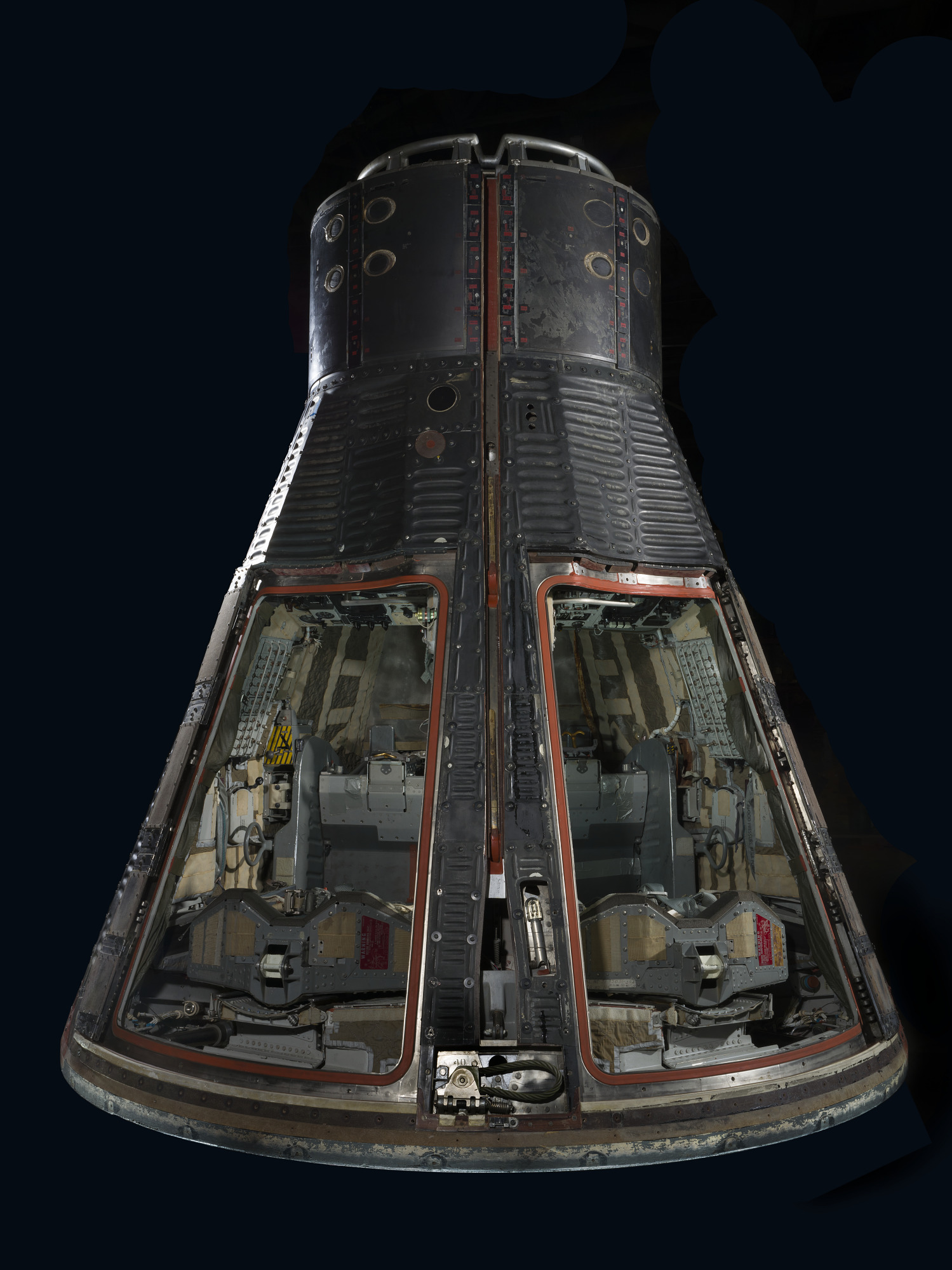 Dark Gemini VII capsule with both hatches removed, revealing two seats and crowded instrument panels.