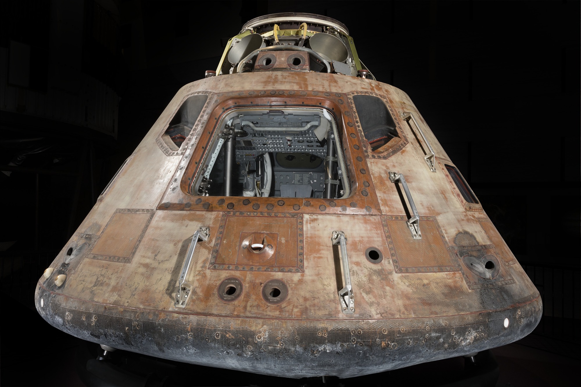 Conical Apollo command module with heat-darkened exterior, open hatch, two windows, and a compact three-person interior.