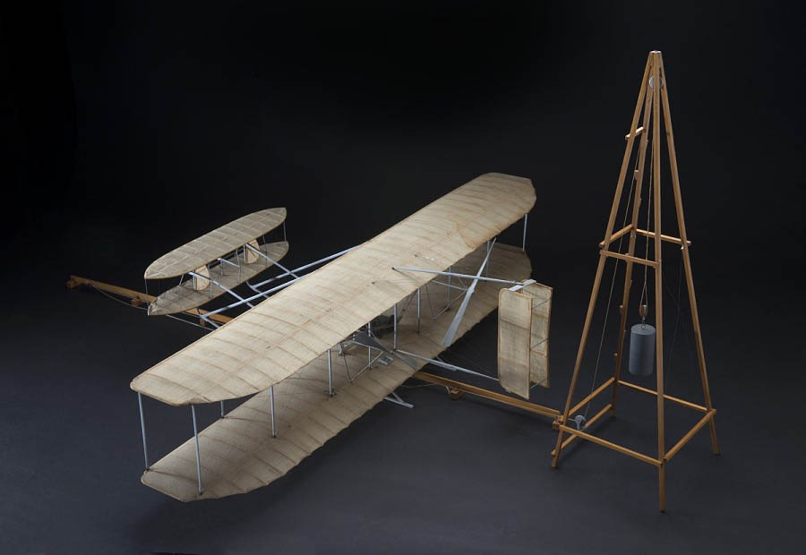 Scale models of Wright gliders and powered aircraft showing fabric wings, forward elevators, rear rudders, launch equipment, and changing control arrangements.
