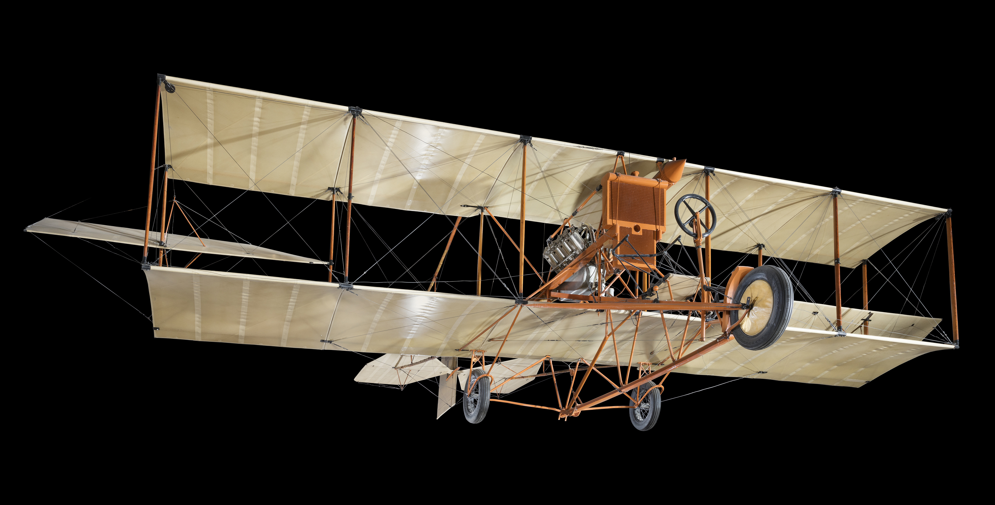 A boxy fabric-covered pusher biplane with orange struts, rear-mounted propeller, tricycle landing gear, and no forward elevator.