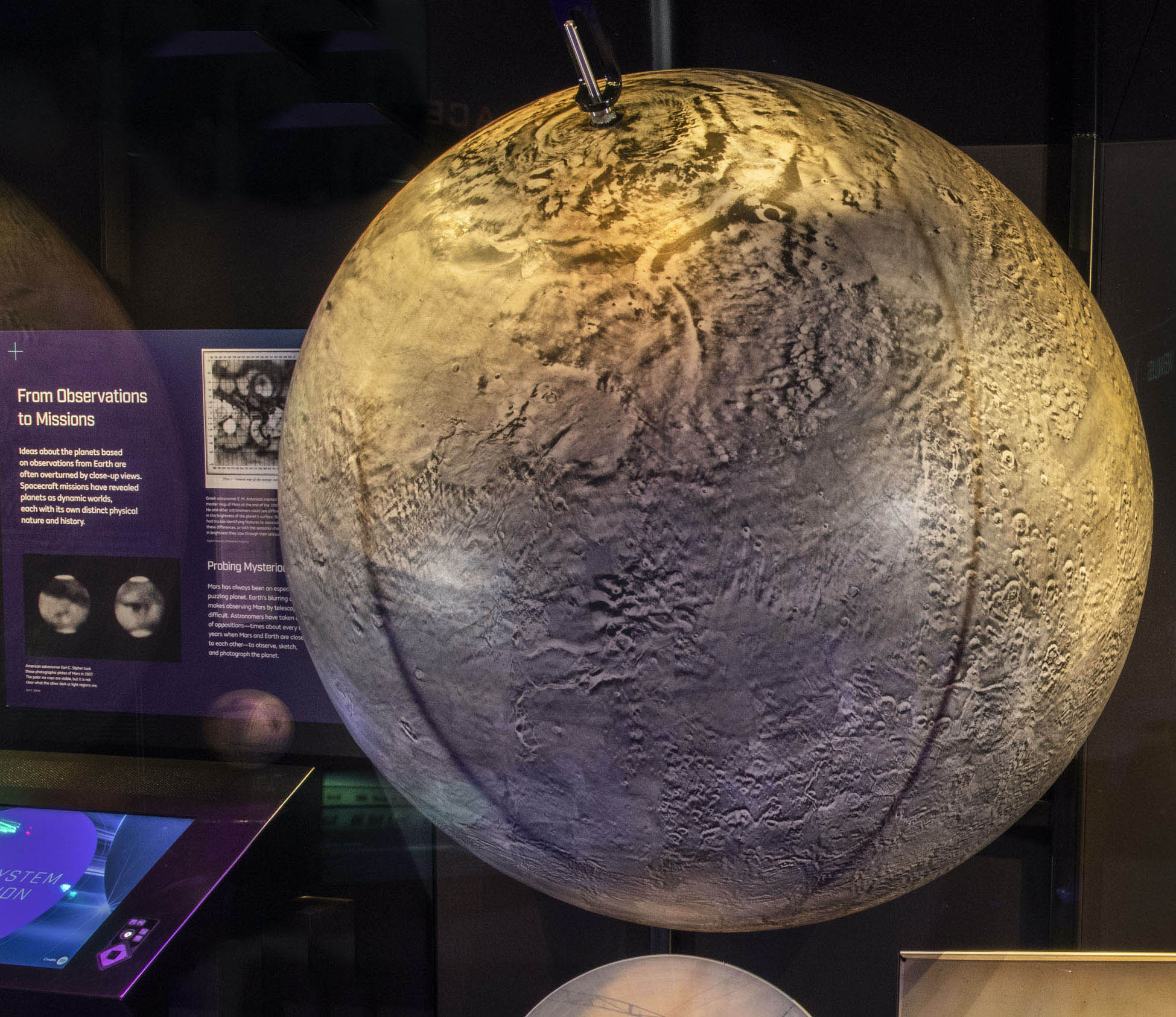 Large gray-brown globe assembled from Mariner 9 photographs, with major Martian canyons and volcanoes visible.