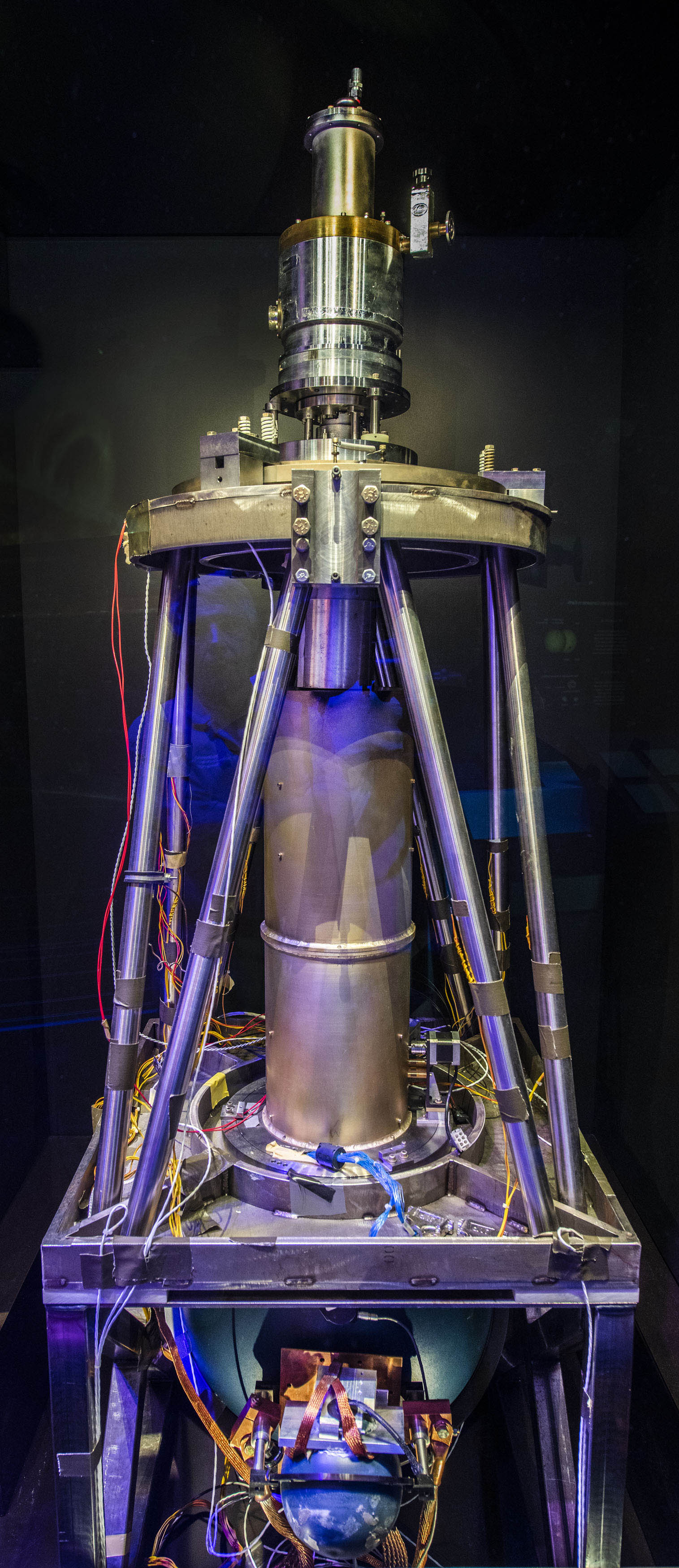 Large open metal instrument with electronics in a rectangular base, a central cylinder, circular detector platform, and angled support braces.