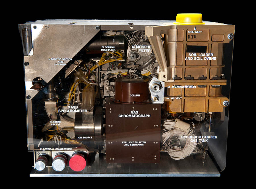 Square instrument package containing labeled chambers, tubing, valves, electronics, and sample-analysis components.