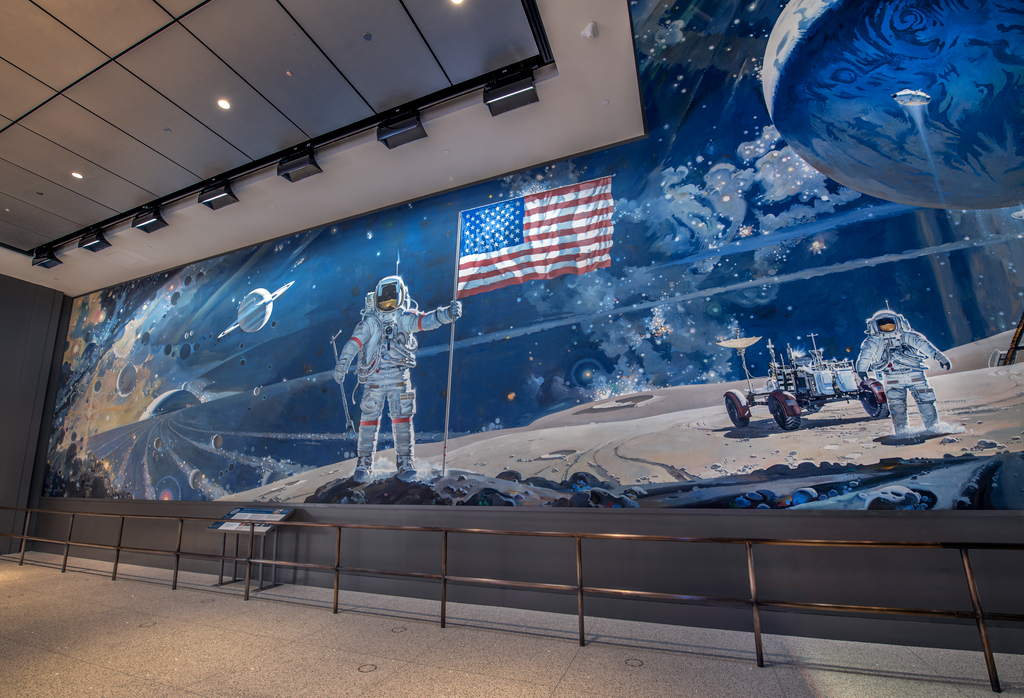 A wall-size mural showing the universe’s birth, planets and asteroids, Apollo astronauts on the Moon, a lunar module and rover, Earth, the Sun, and deep space.