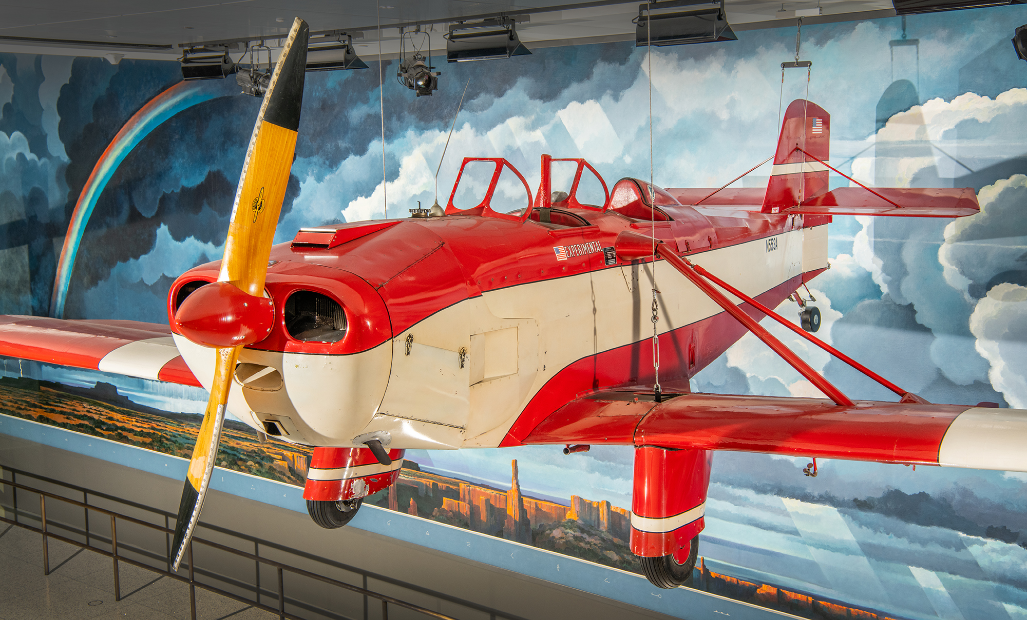 A small red-and-white single-engine propeller airplane with two open cockpit seats and wings designed to fold for storage and towing.
