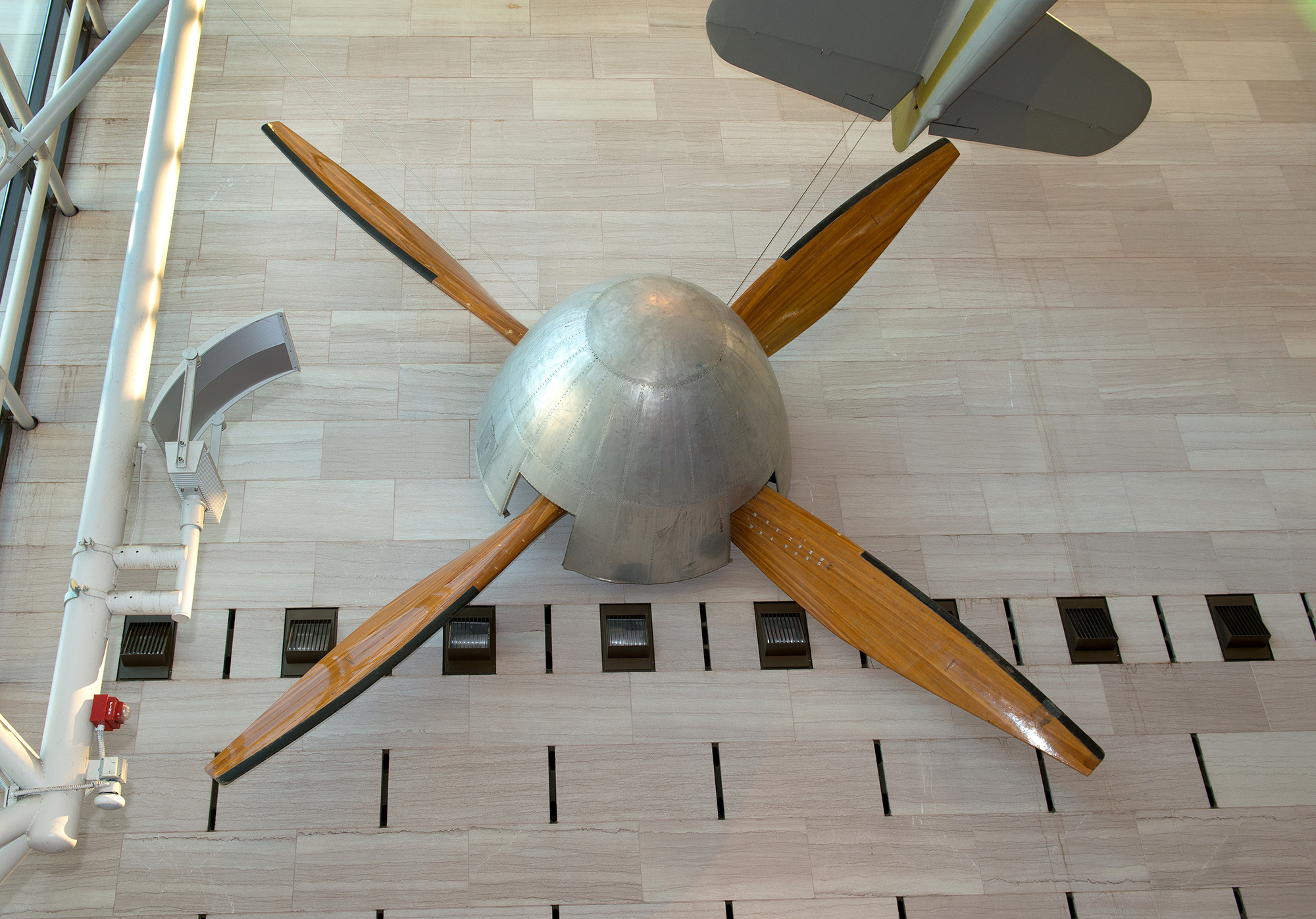 A massive four-bladed fan with a wooden central hub and long silver metal blades, built to move air through a full-scale wind tunnel.