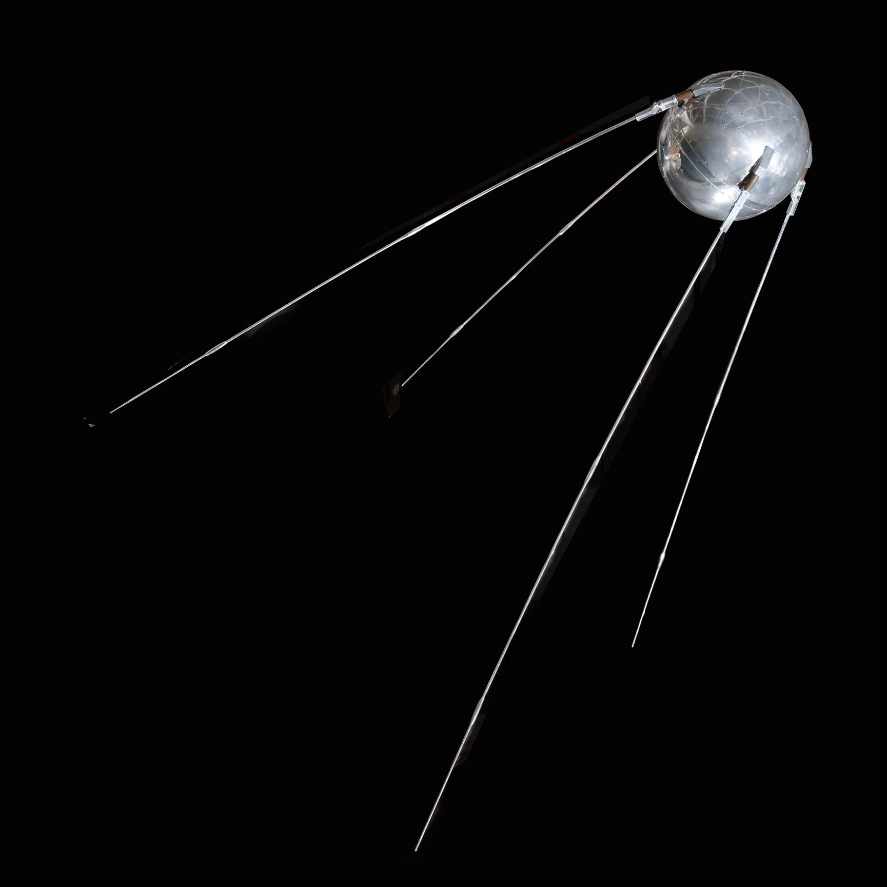 A polished spherical satellite with four long trailing antennas, displayed beside the slender Explorer I satellite.