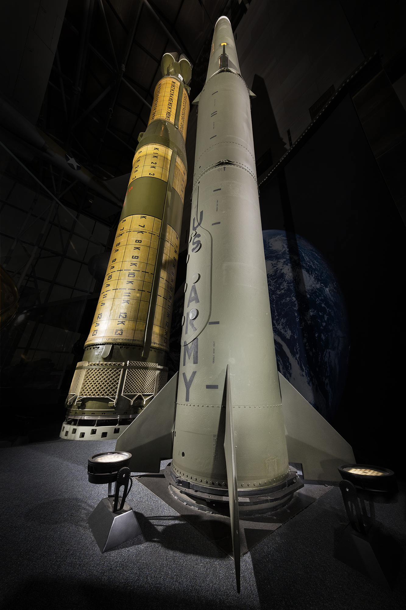 A large olive-green Soviet intermediate-range ballistic missile with gold-colored bands and numbered markings, displayed beside a U.S. Pershing II.