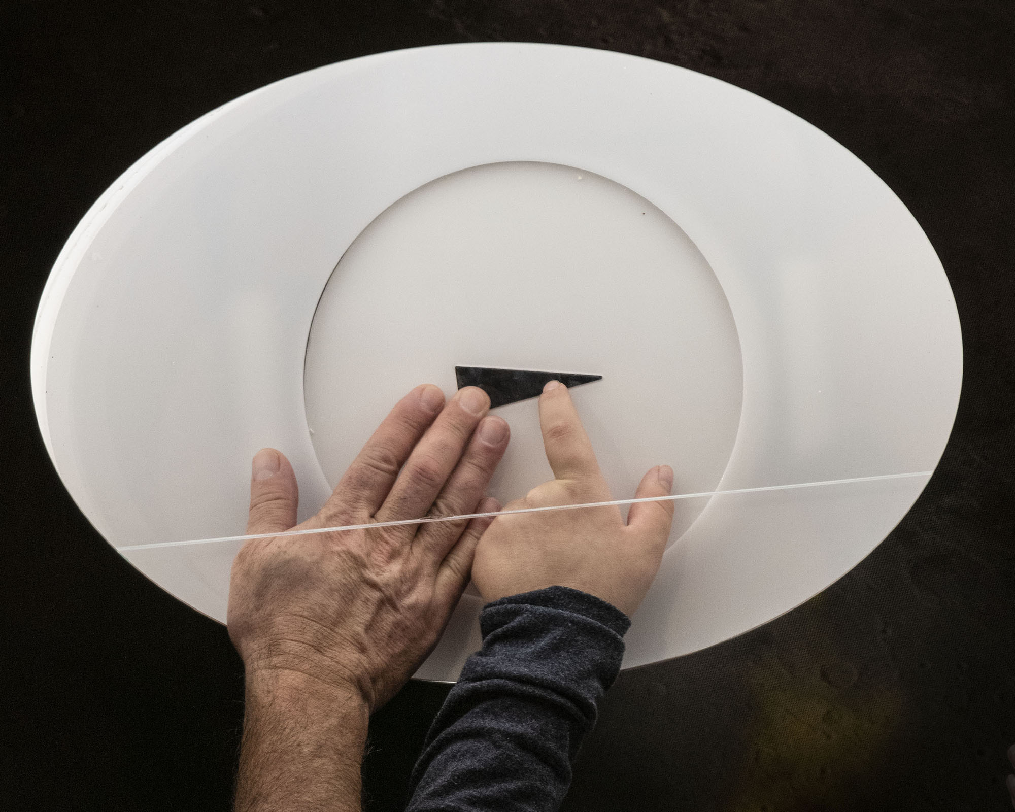 A triangular piece of dark lunar basalt embedded in white protective material beneath clear acrylic, with one surface exposed so visitors can touch it.
