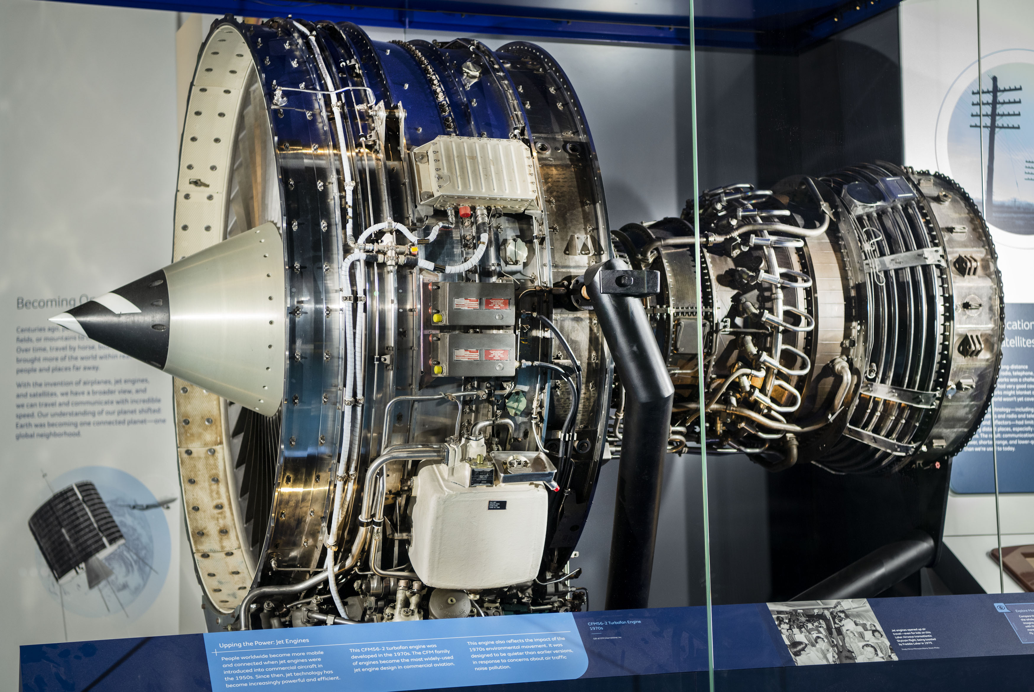 Metal turbofan displayed in cutaway form so its fan, compressor, combustion section, turbine, and exhaust path can be seen.