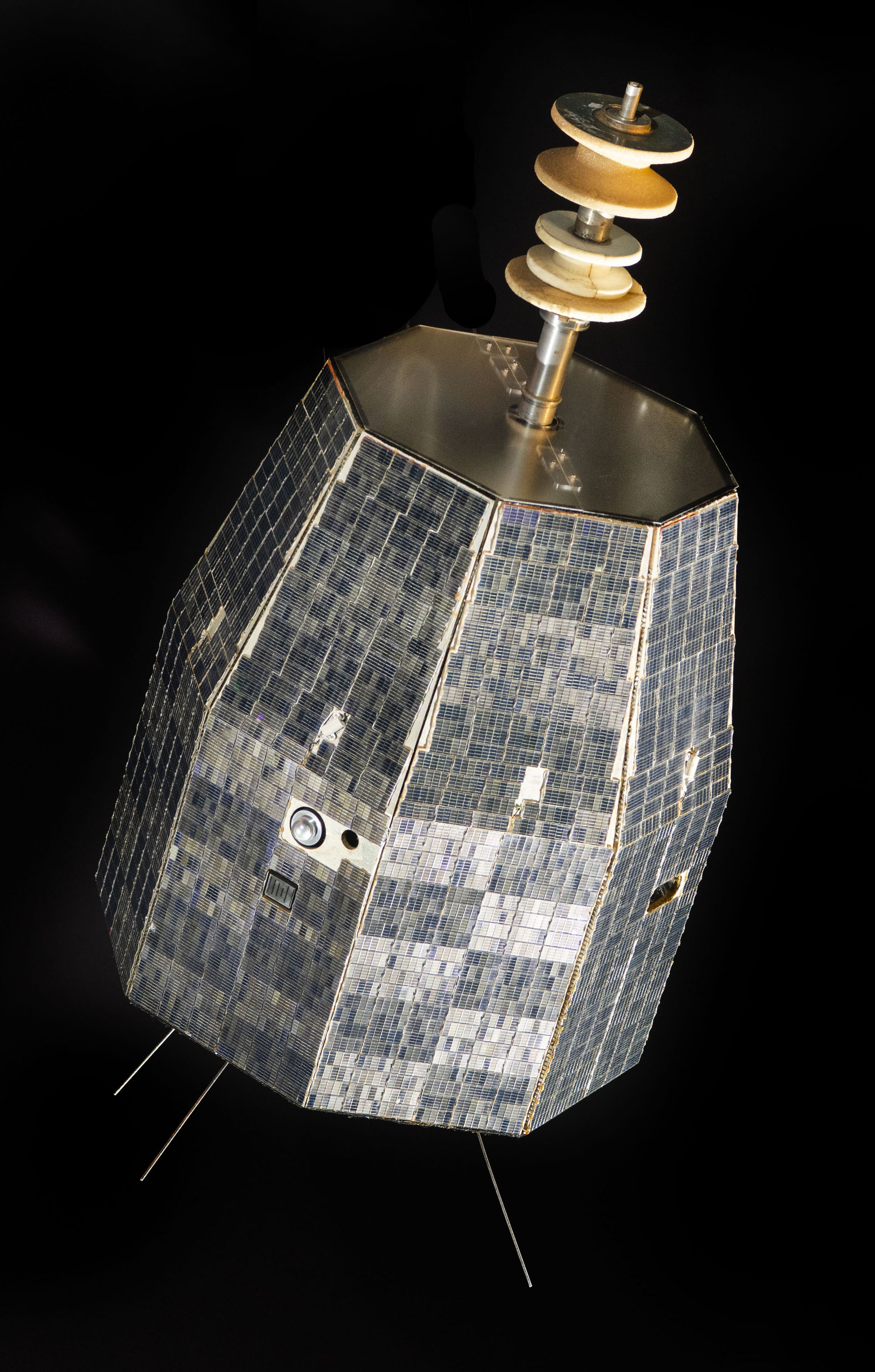 Solar-cell-covered octagonal communications satellite with a thick upper antenna and thin telemetry antennas at its base.