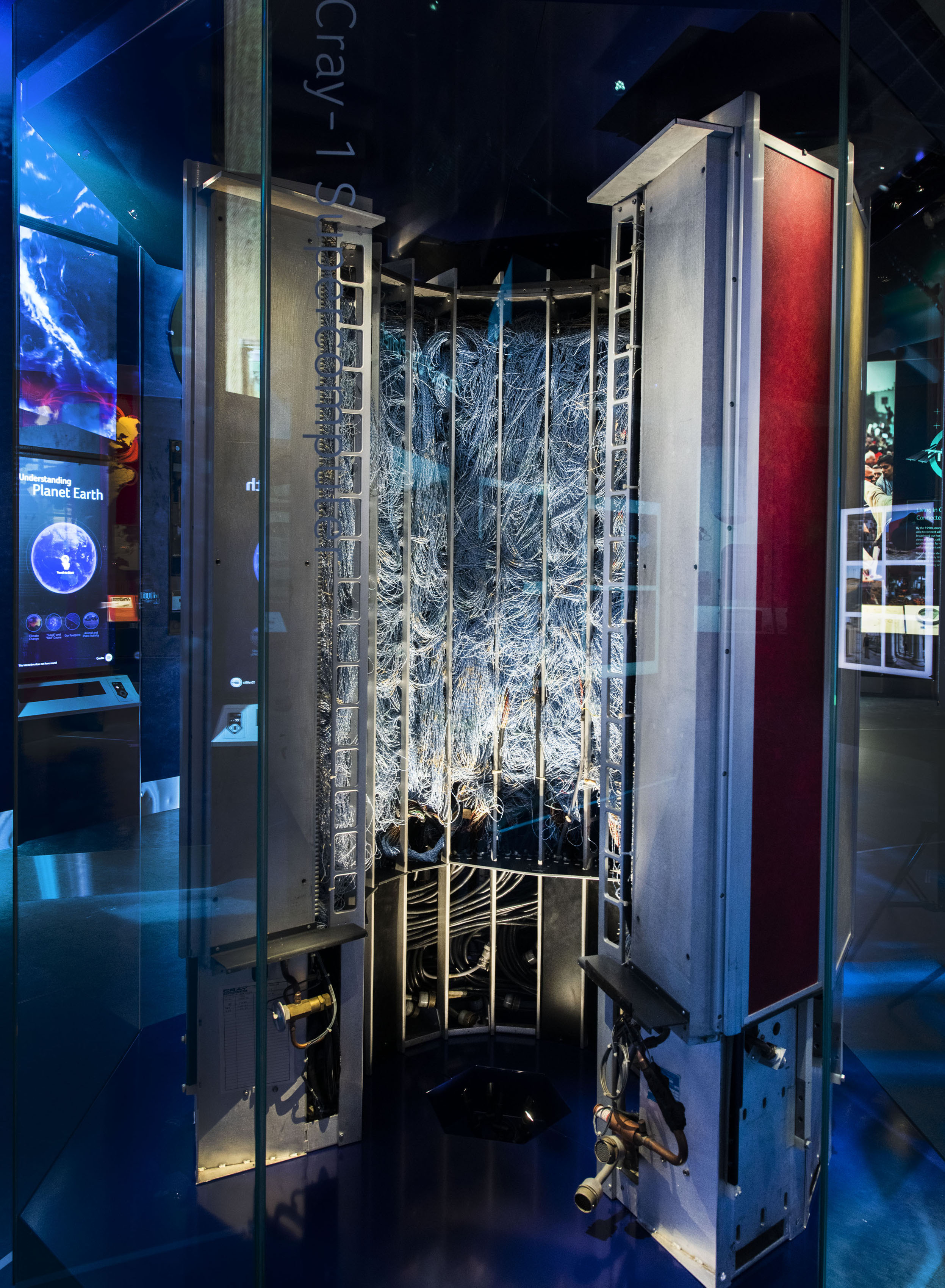 Curved computer cabinet with exposed circuit boards and wiring, surrounded by red, cream, and blue padded panels.