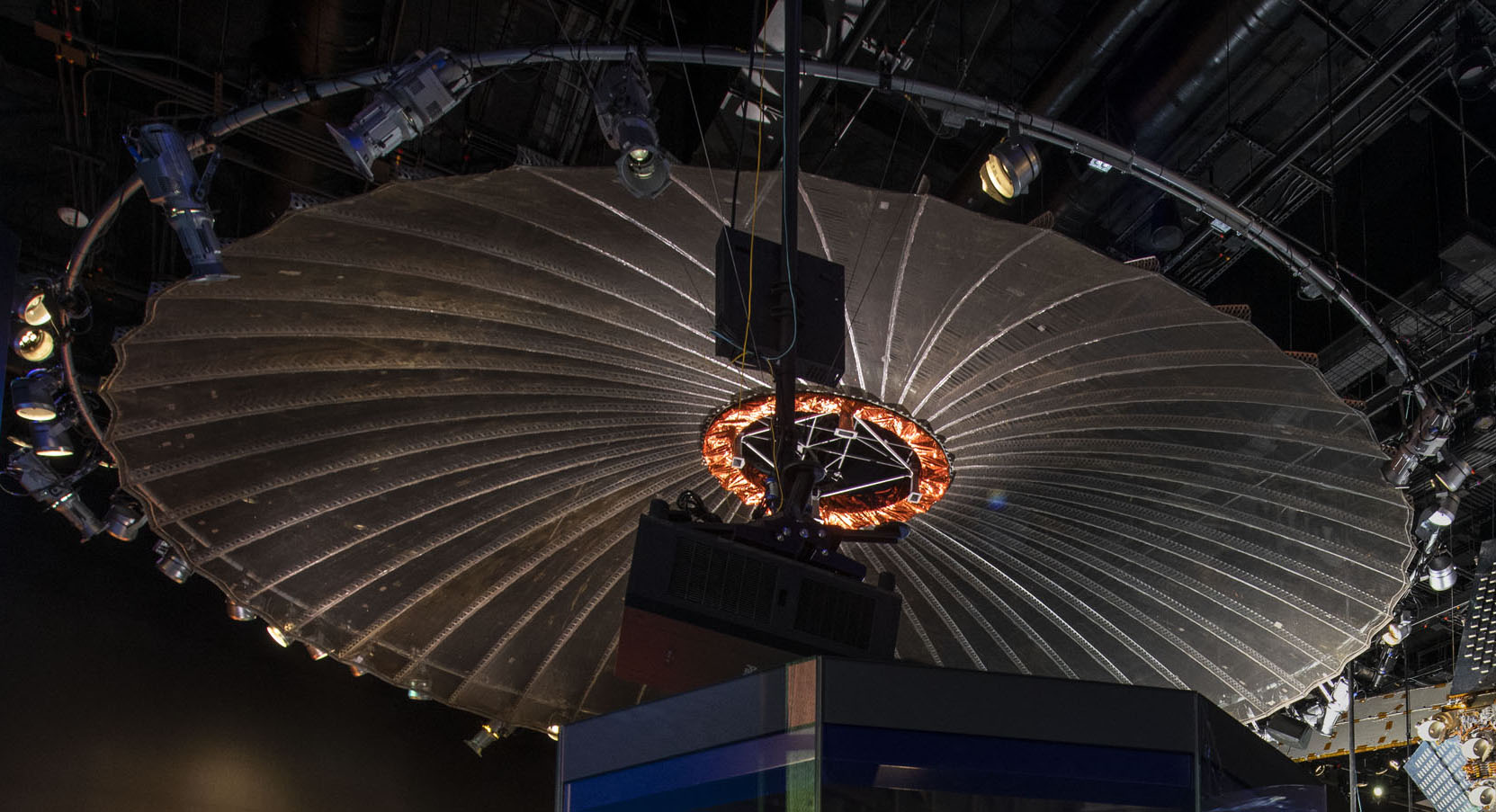 Large parabolic mesh antenna attached to a metallic ring and displayed open like an umbrella.
