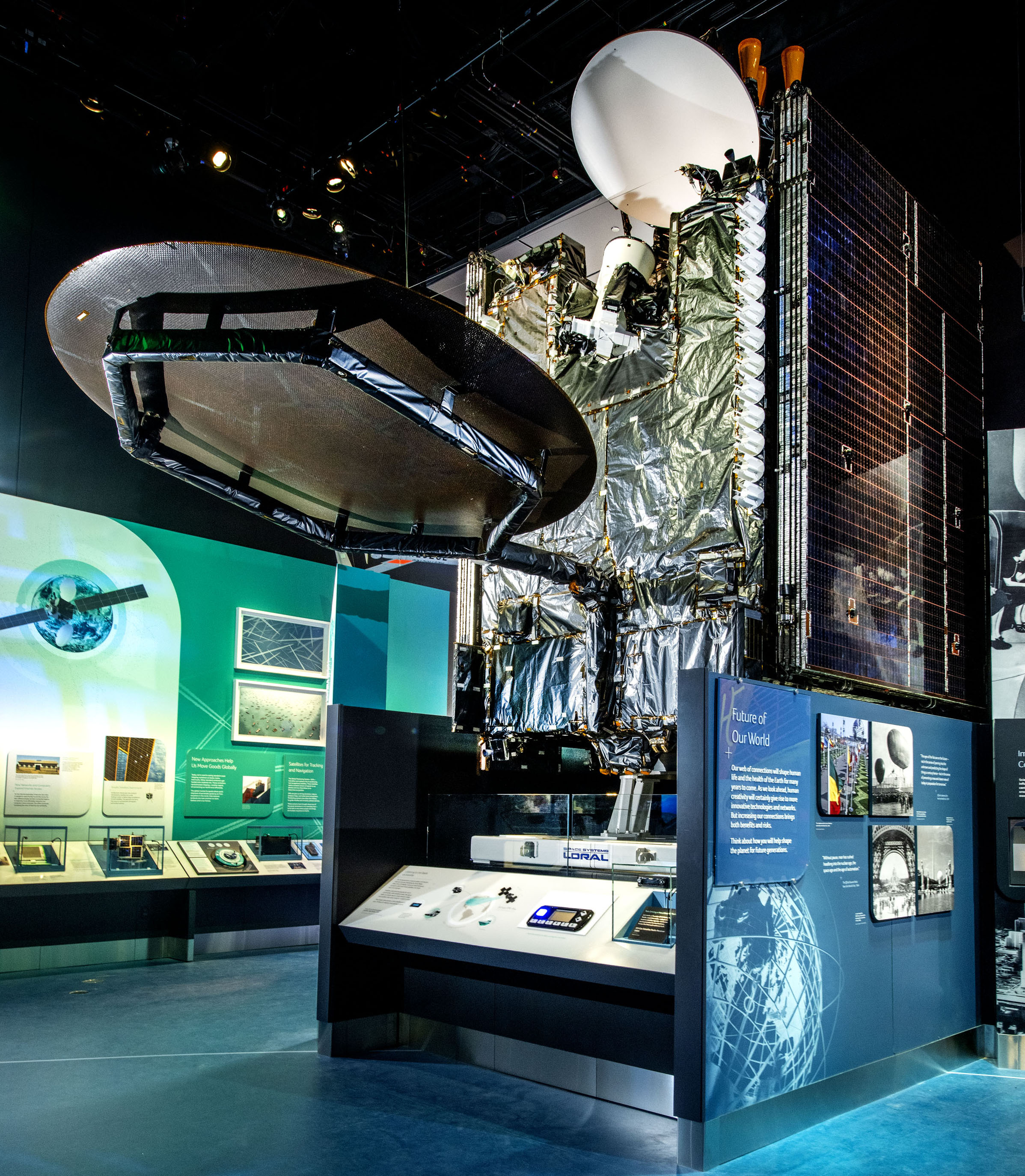Large box-shaped communications satellite wrapped in reflective material with a round antenna and folded solar arrays.