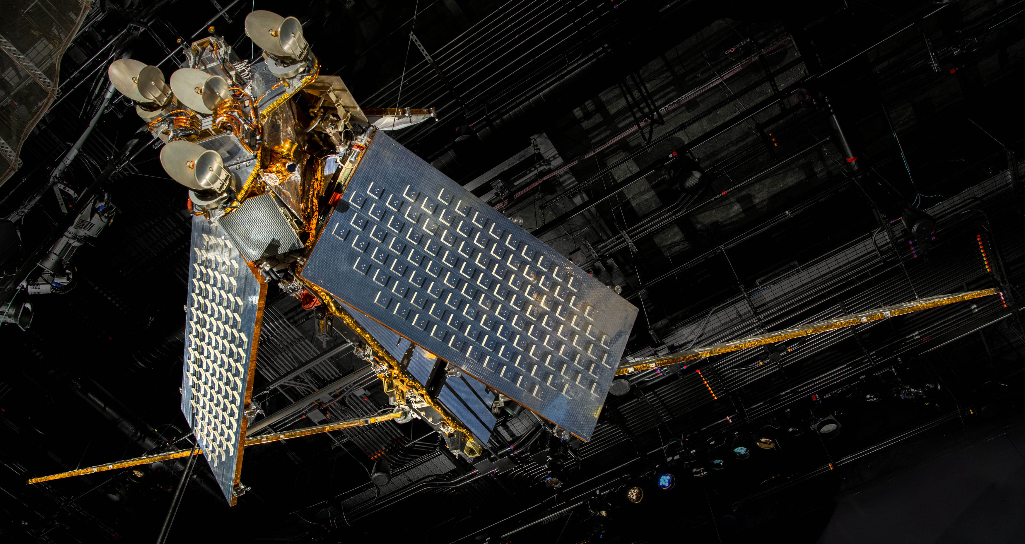 Large metal communications satellite with two broad silver structures angled outward like wings.