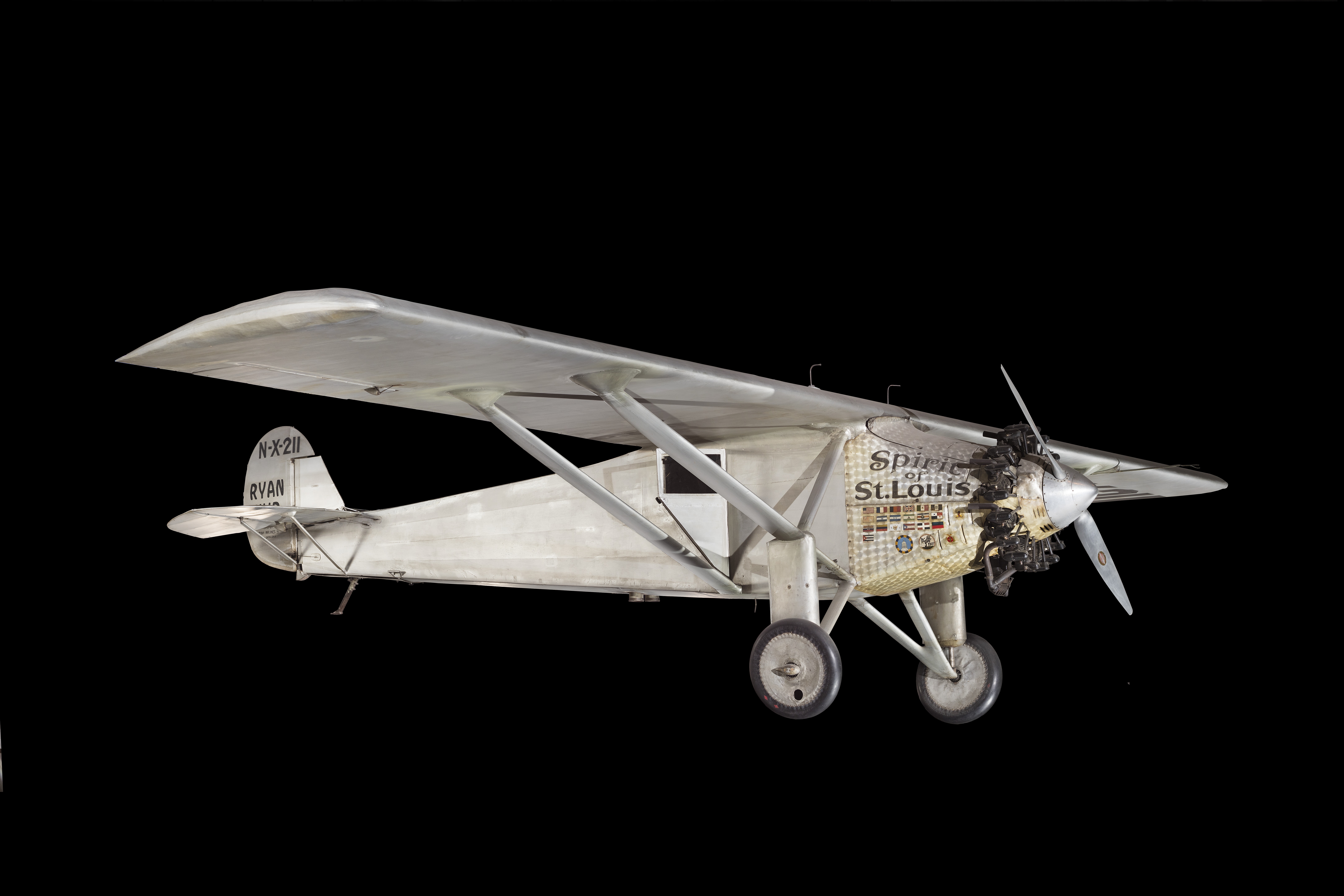 Silver, fabric-covered Ryan monoplane with a high wing, radial engine, and no forward cockpit window.