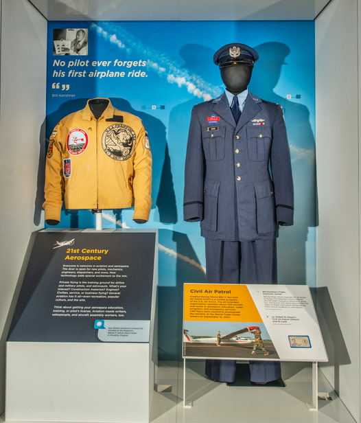 Yellow flight jacket with a name tag and several aviation and aerobatic patches.