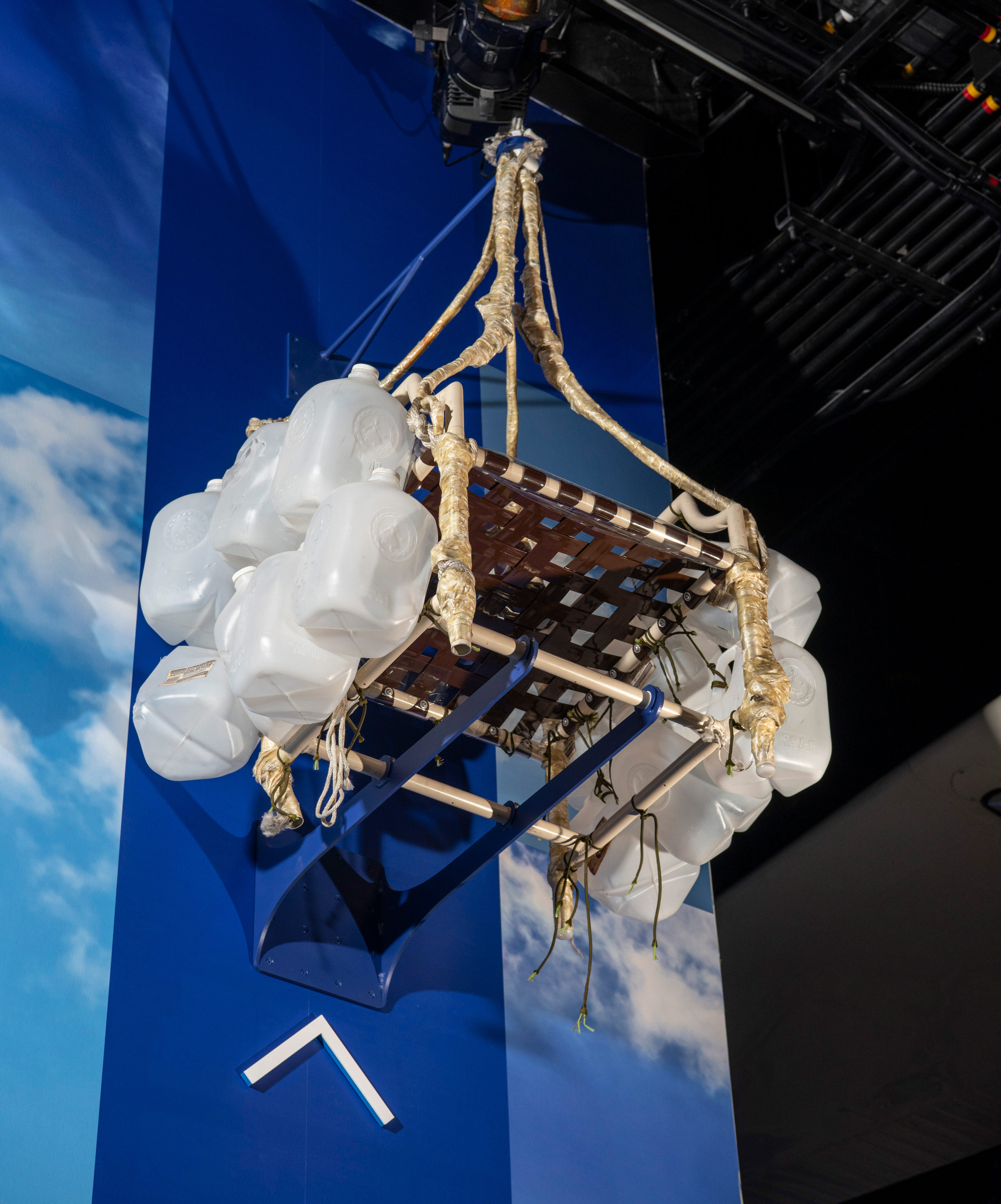 Aluminum lawn chair with woven straps, water jugs, ropes, and equipment used beneath weather balloons.