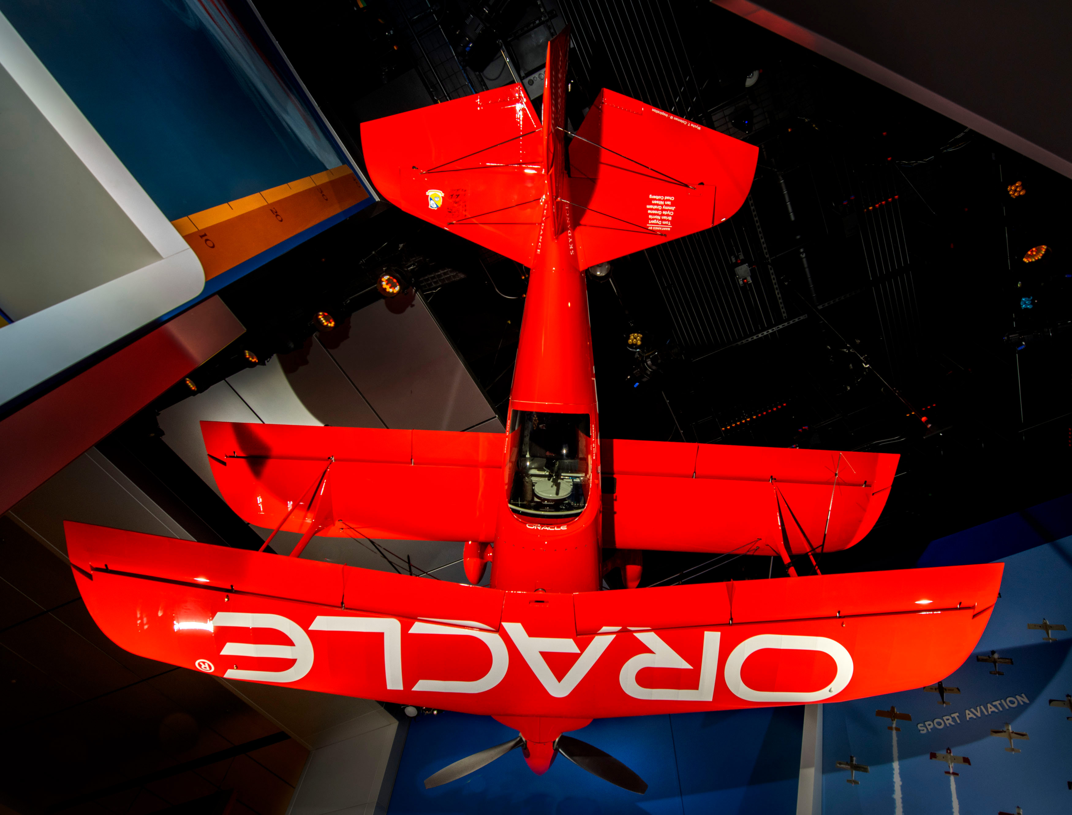 Red single-seat aerobatic biplane with eight ailerons, curved wingtips, sponsor markings, and a three-blade propeller.