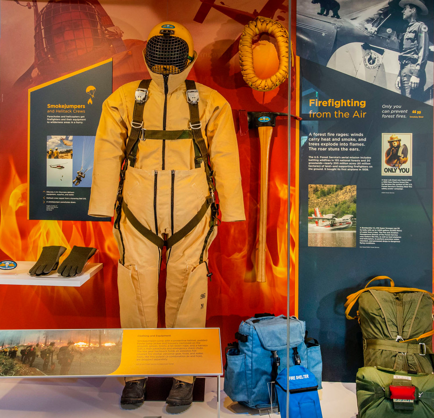 Yellow padded smokejumper suit, protective helmet, harness, parachutes, pack, rope, gloves, boots, and firefighting tools.