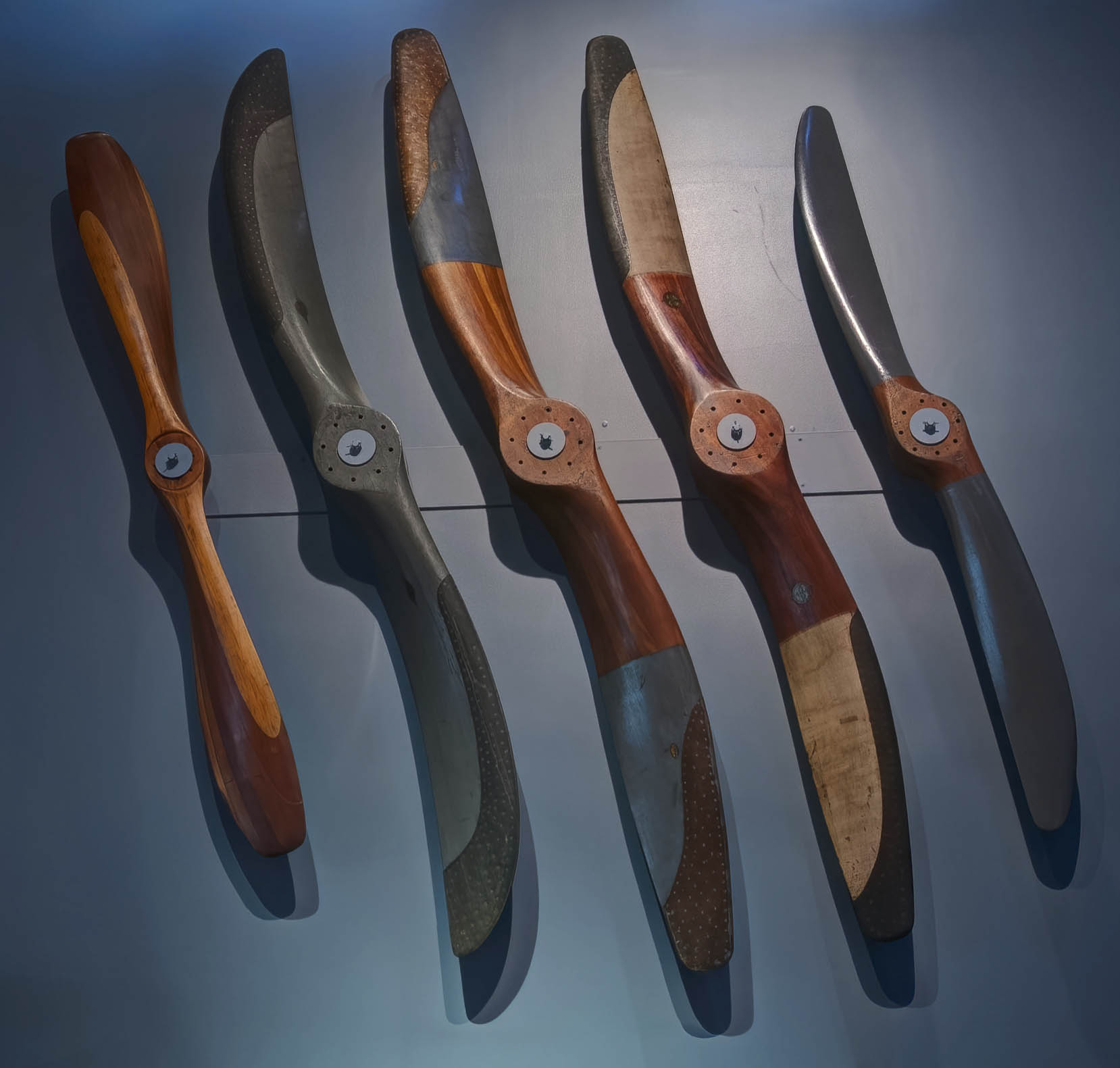 Five laminated wooden aircraft propellers mounted vertically above exhibit cases.