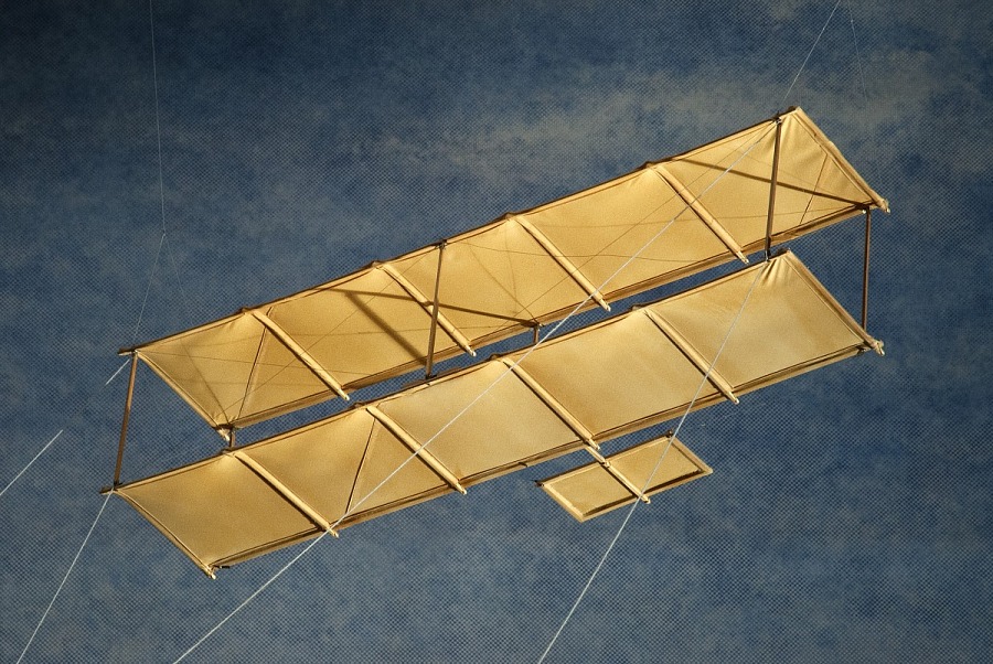 Fabric-covered wooden biplane kite with upper and lower wings, a forward canard, and control lines for twisting the wings.