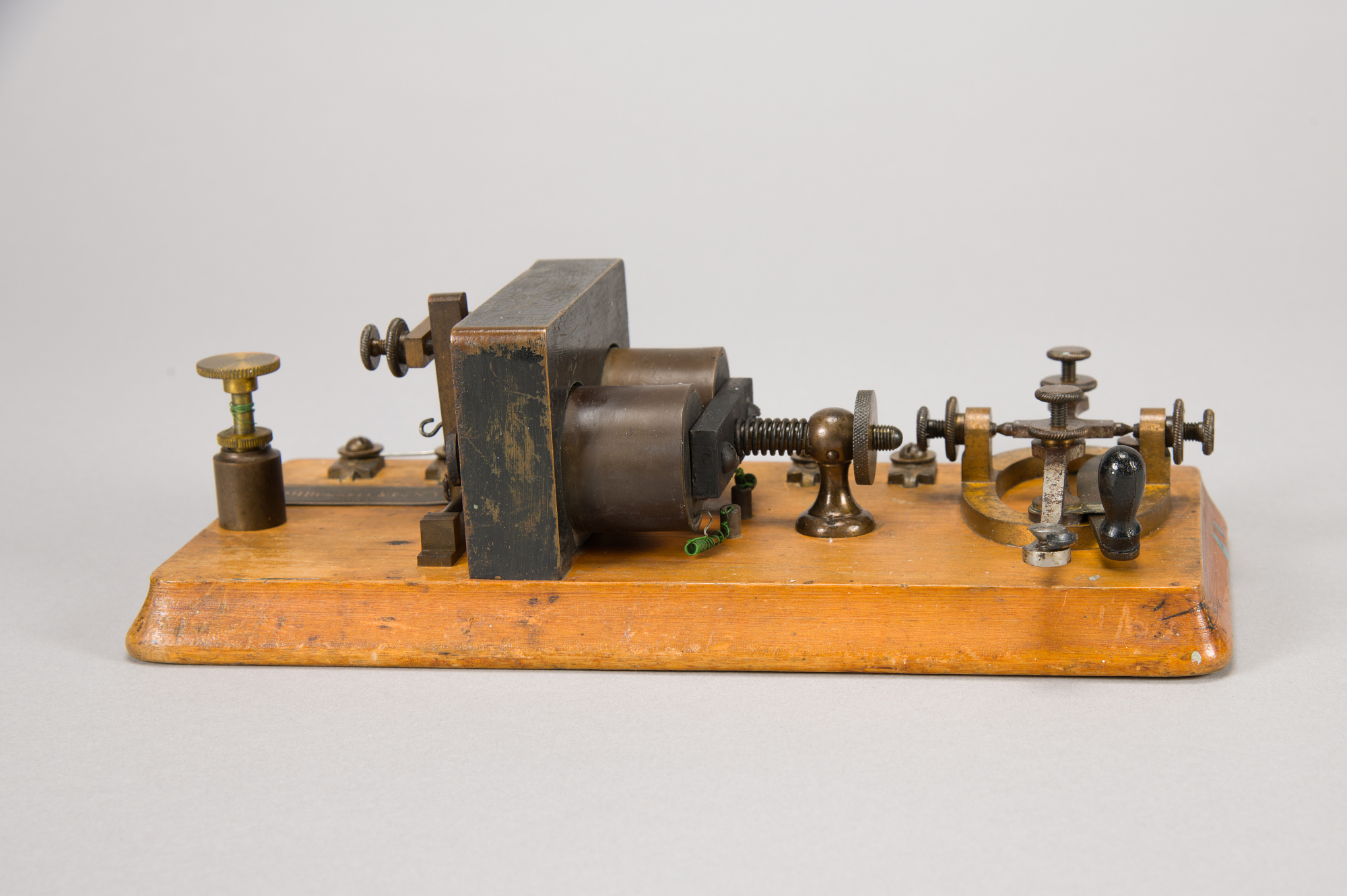 Telegraph key on a light pine base with a dark metal lever, sounder hammer, and wiring mounted underneath.