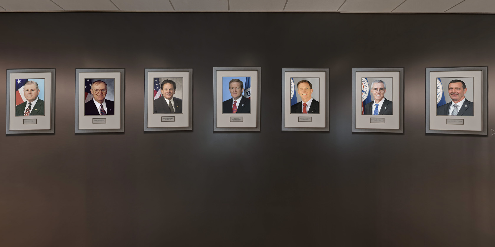 Formal portraits of Transportation Security Administration leaders arranged along a gallery wall